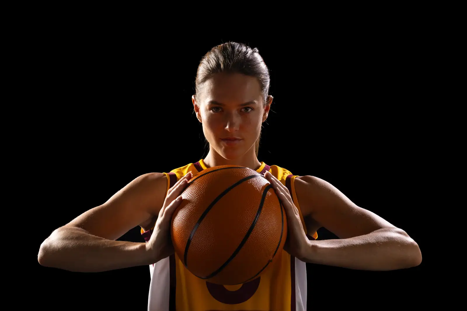 Basketball player holding the ball at chest height against a dark background