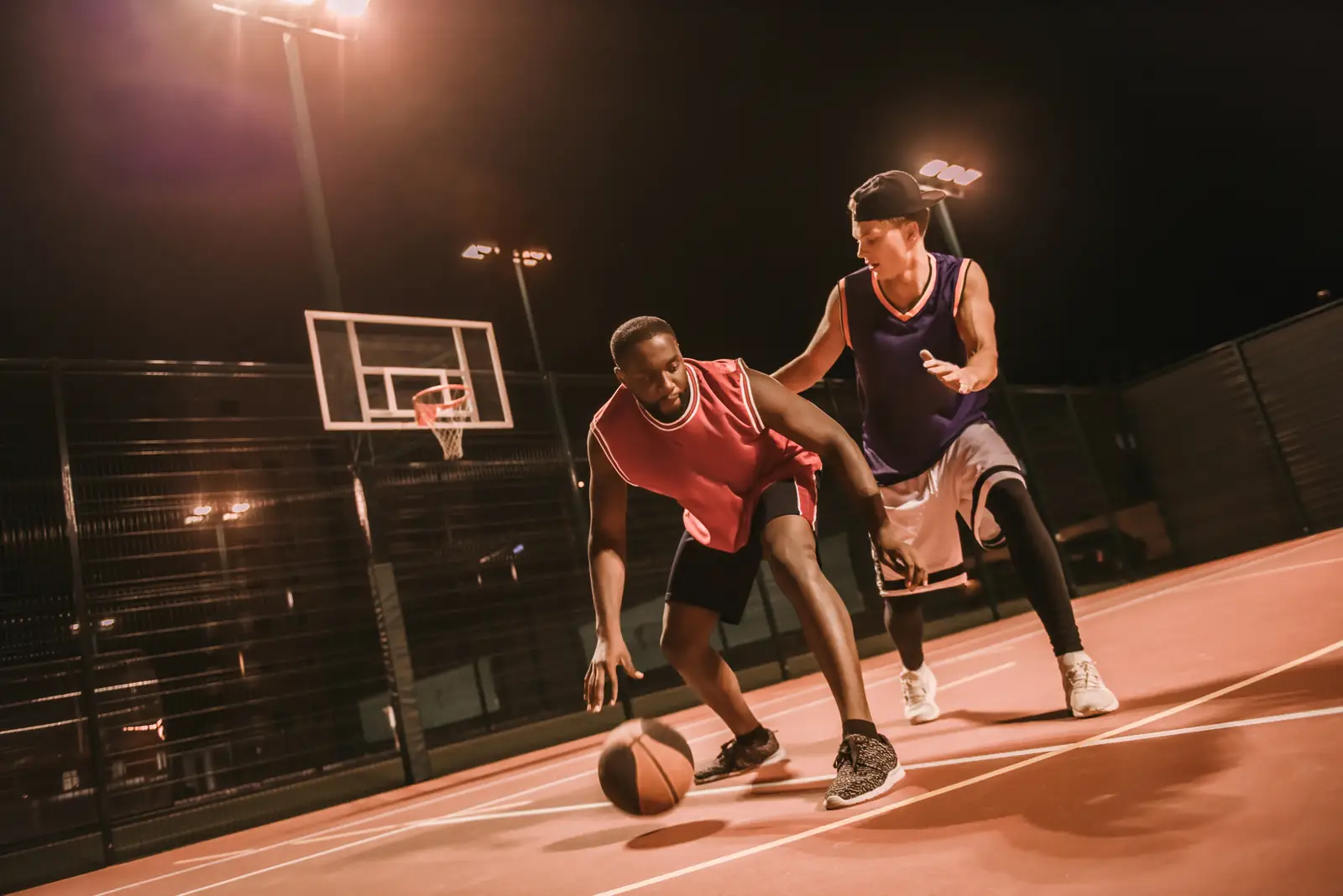 Two basketball players going one-on-one on an outdoor court at night