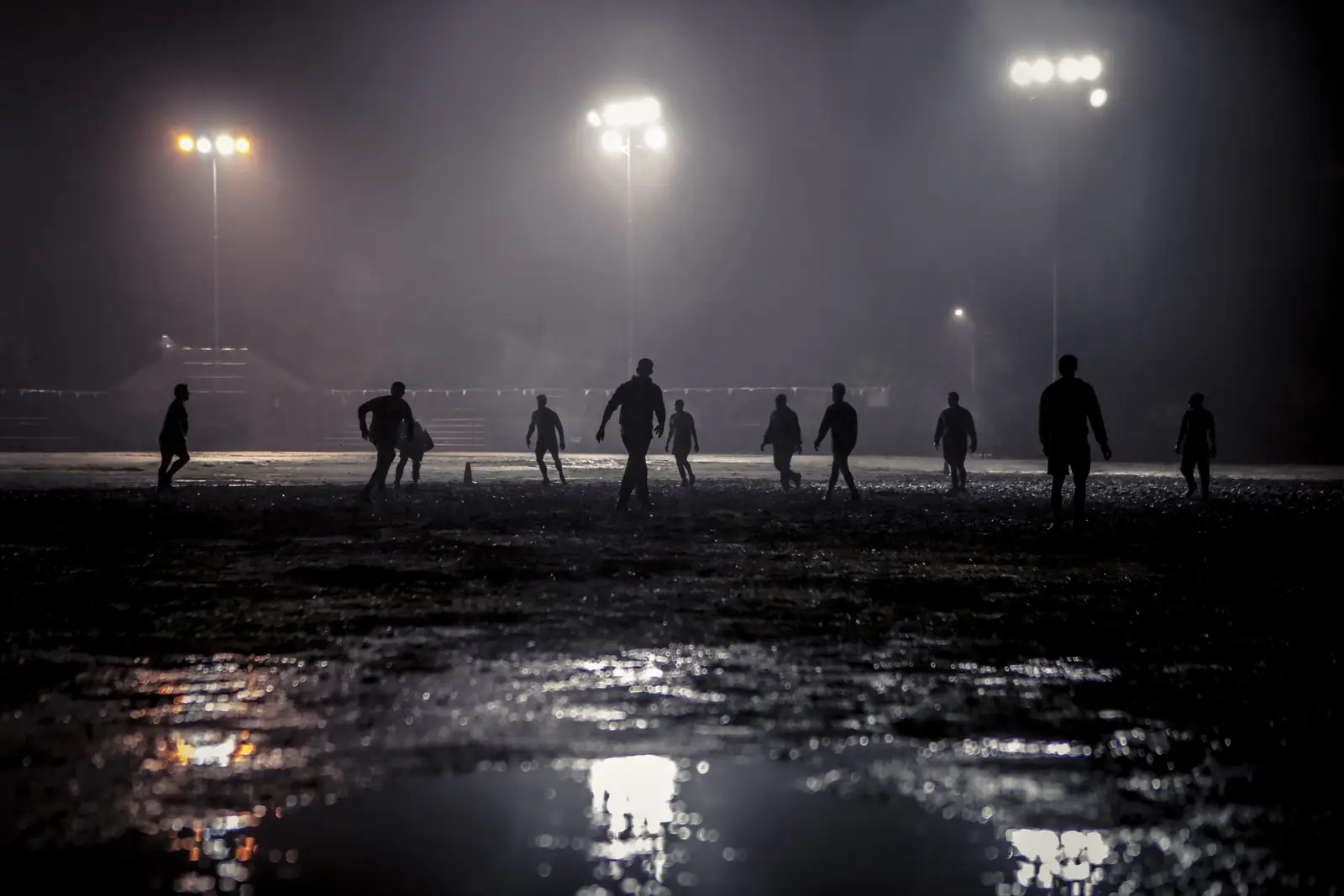 Amateur football match under floodlights on a wet pitch at night