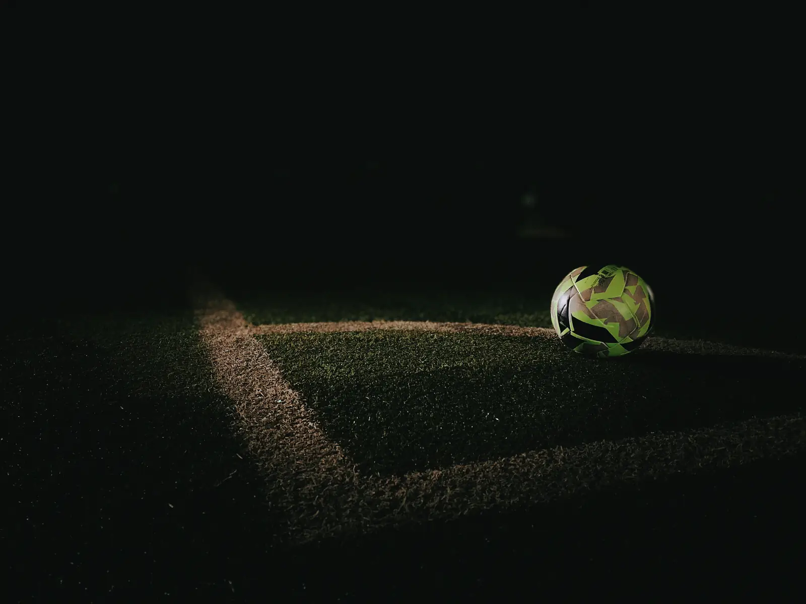 Football resting on the corner of a pitch at night