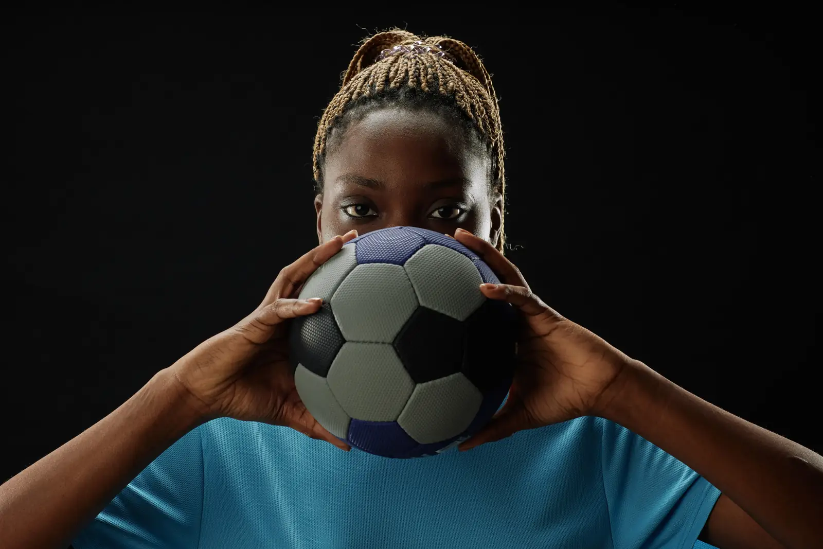 Football player holding a match ball up in front of her face