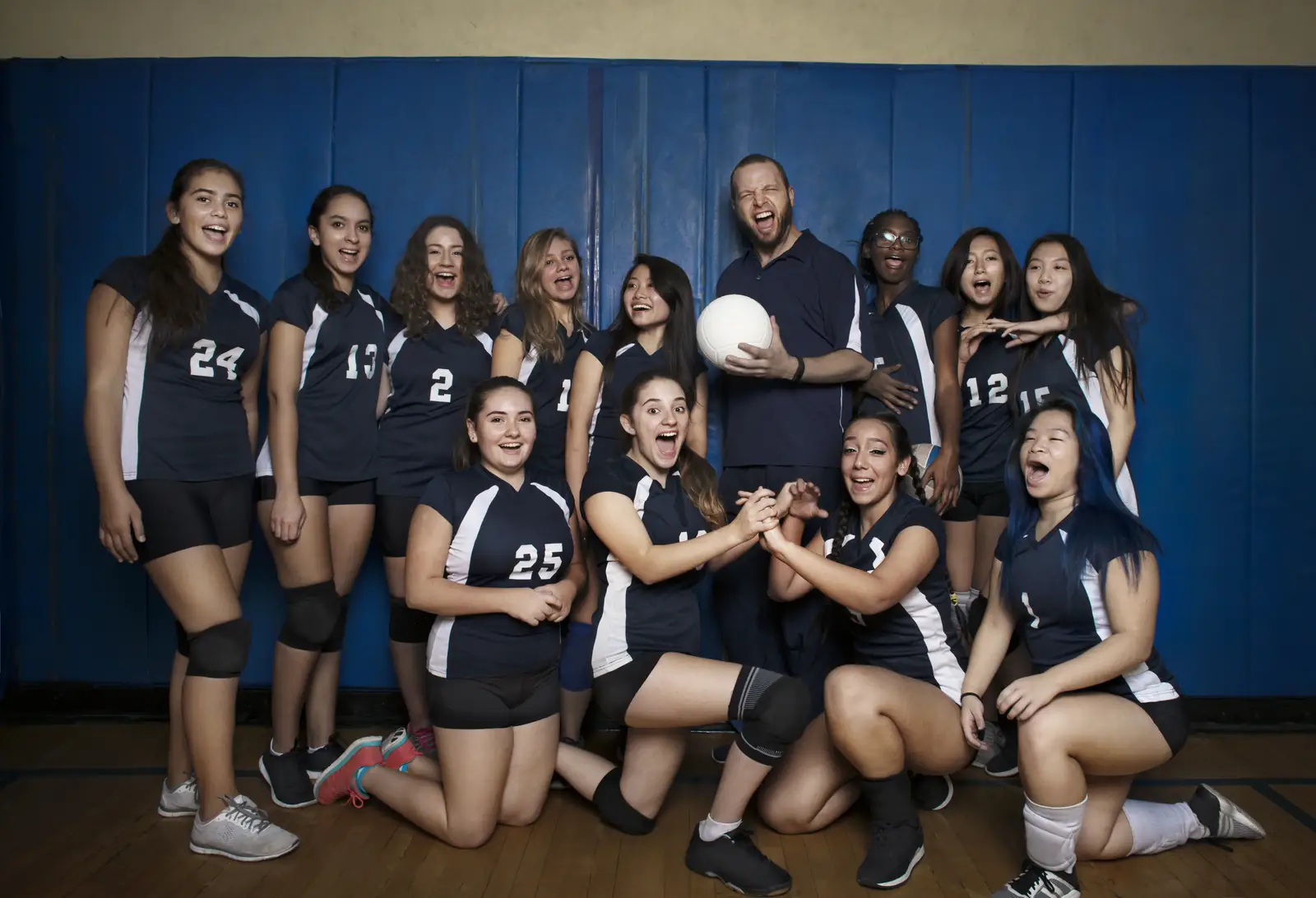 Girls' volleyball team posing with their coach in a school gym