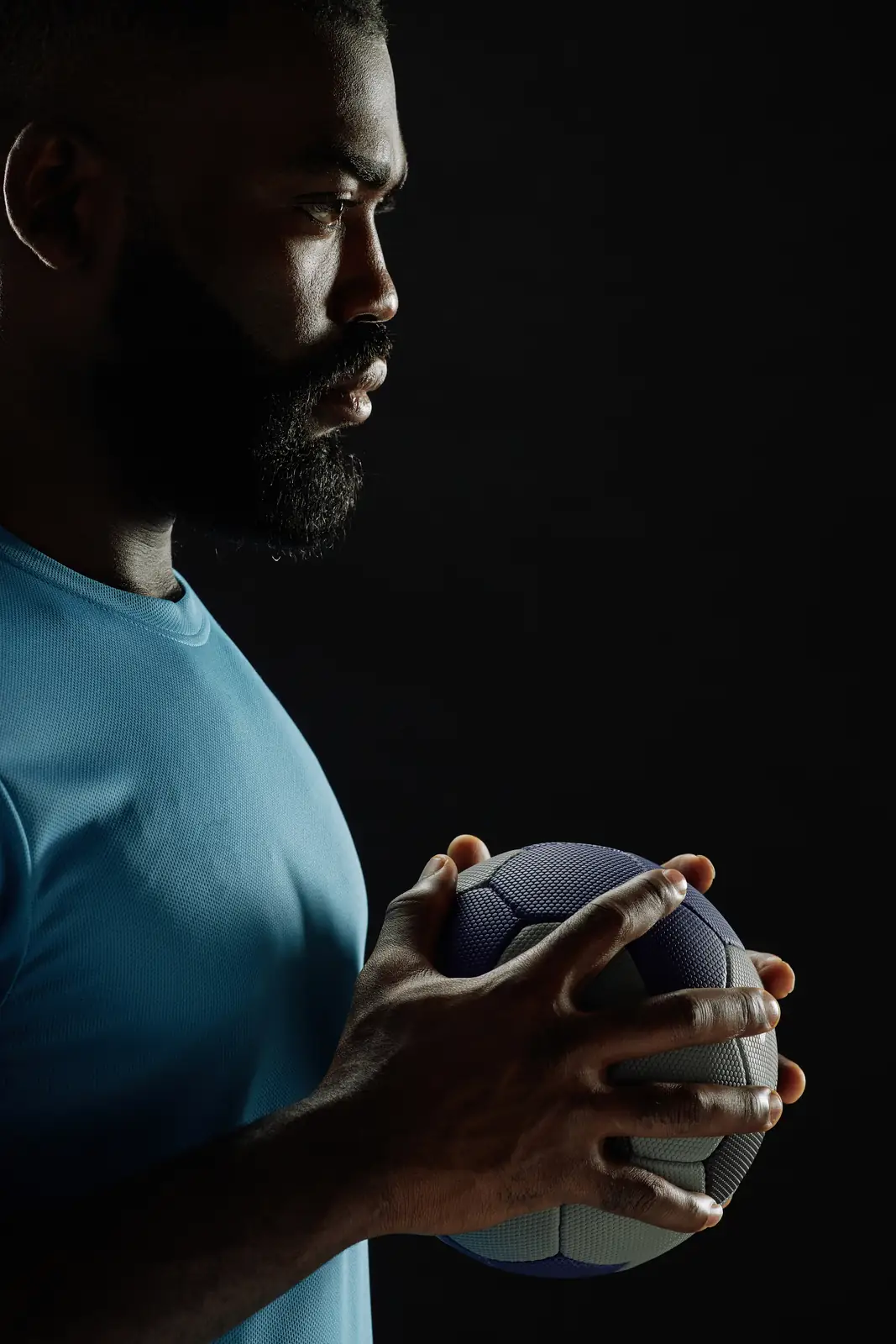 Handball player holding the ball, focused, against a dark backdrop