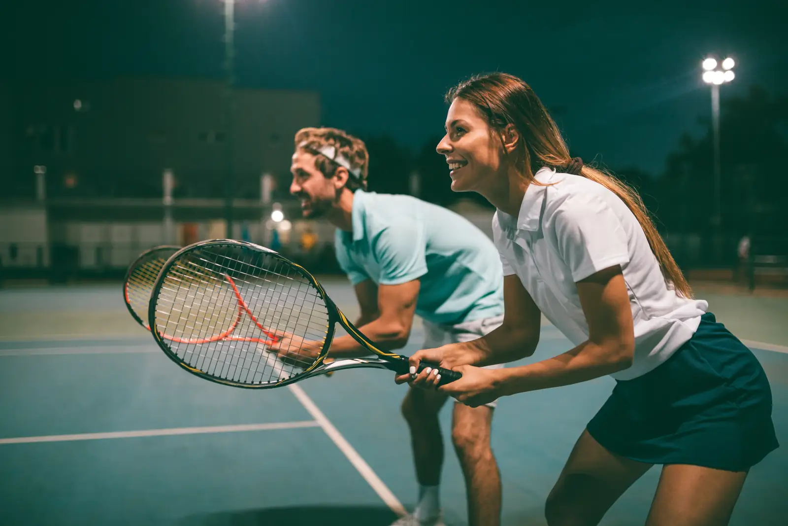 Tennis coach and player smiling during a floodlit lesson