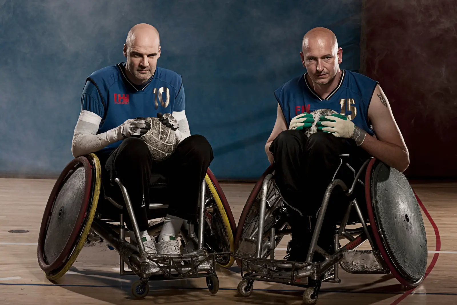 Two wheelchair athletes holding sports balls on an indoor court