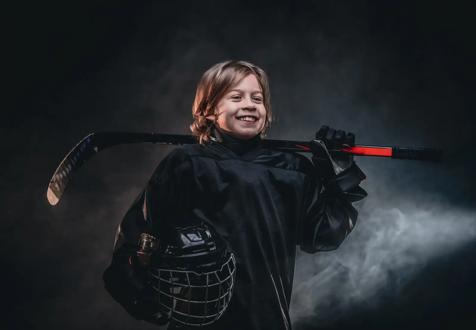 Smiling young hockey player holding his stick and helmet